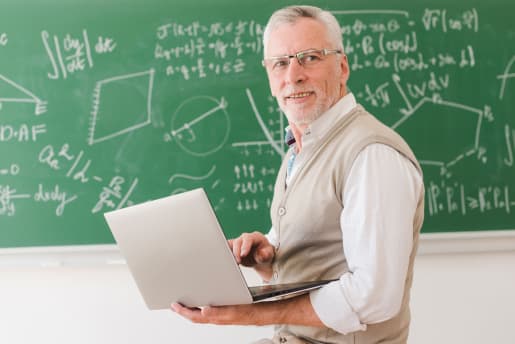 Professor holding a laptop in front of a blackboard